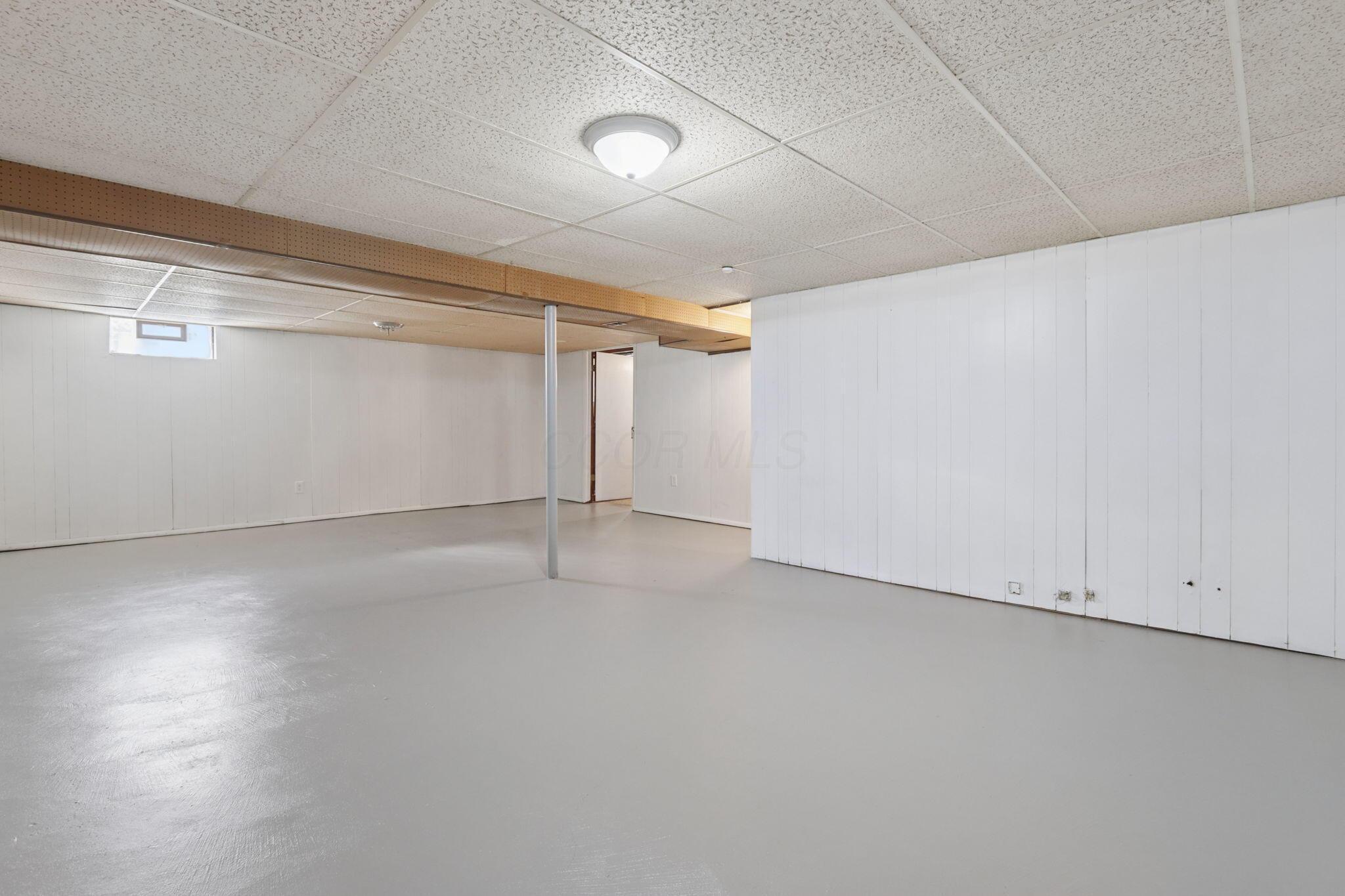 Empty basement with a gray concrete floor, white paneled walls, and a central support post.