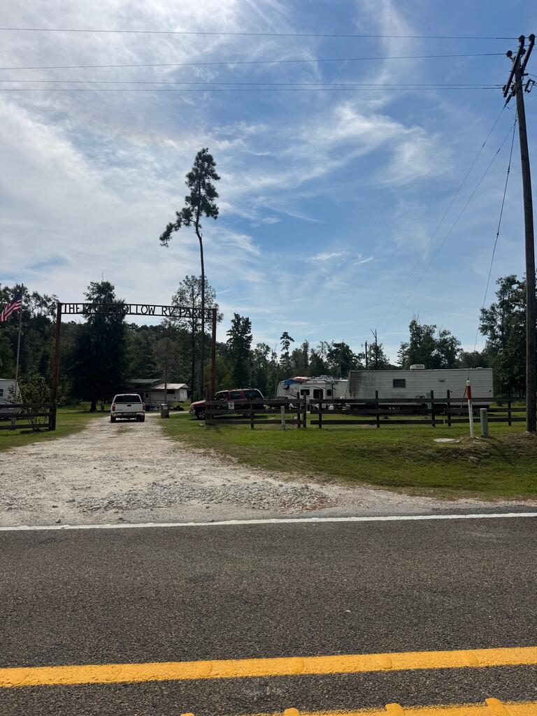 RV park entrance with a gravel driveway, wooden fencing, and parked travel trailers.