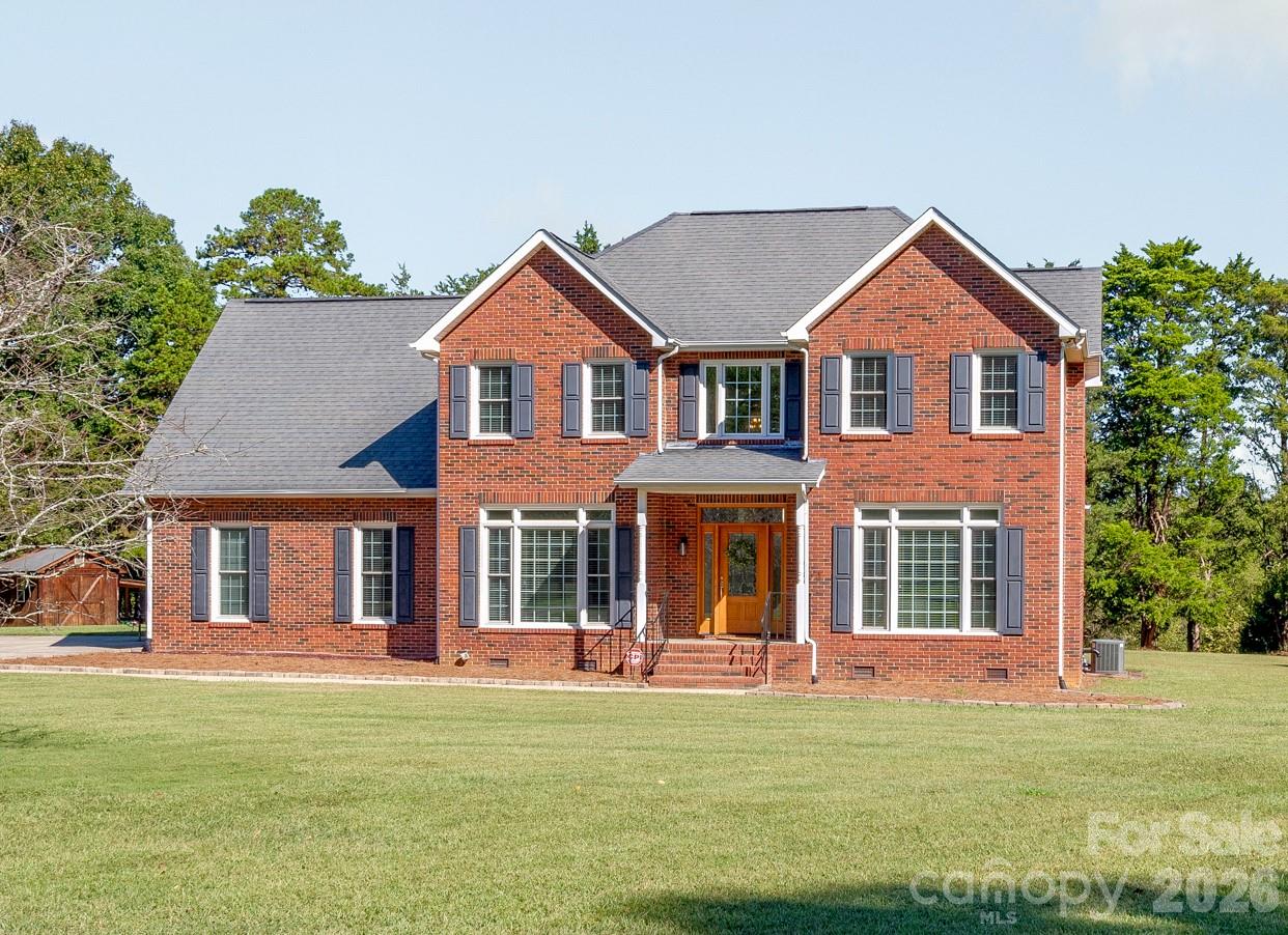 Two-story red brick house with gray shutters, covered entry, attached garage, and broad lawn.