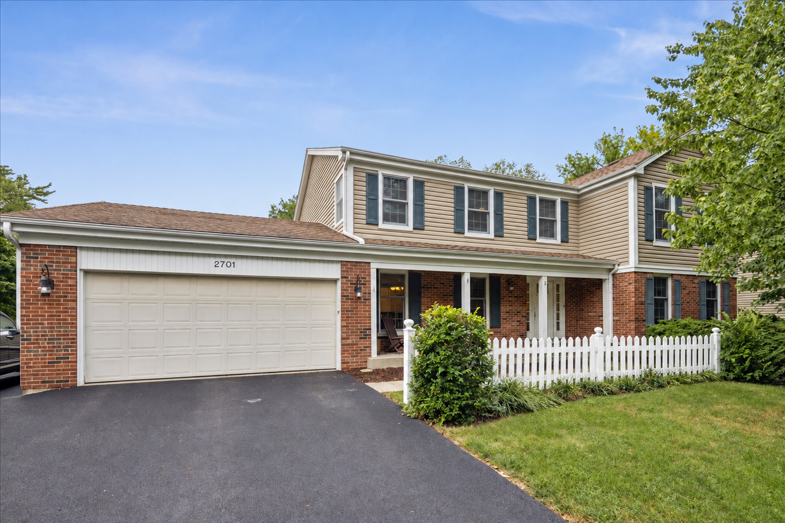 Two-story beige and brick home with a double garage and white picket fence.