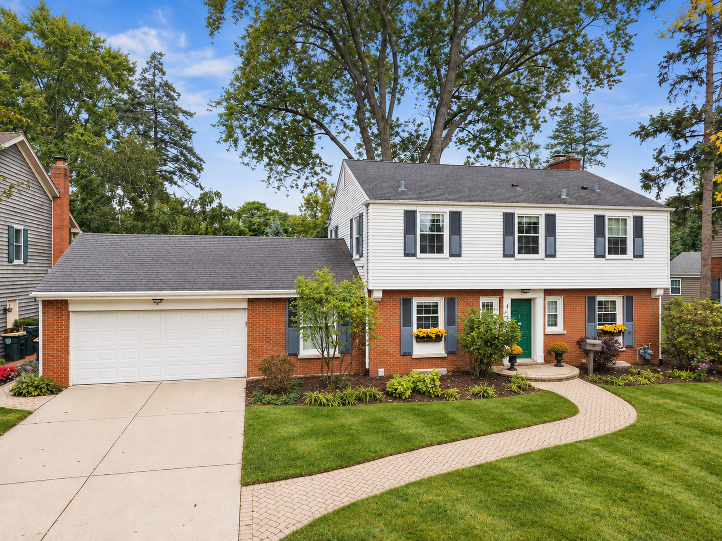 Two-story white-and-brick home with an attached garage and curved brick walkway through the front lawn.