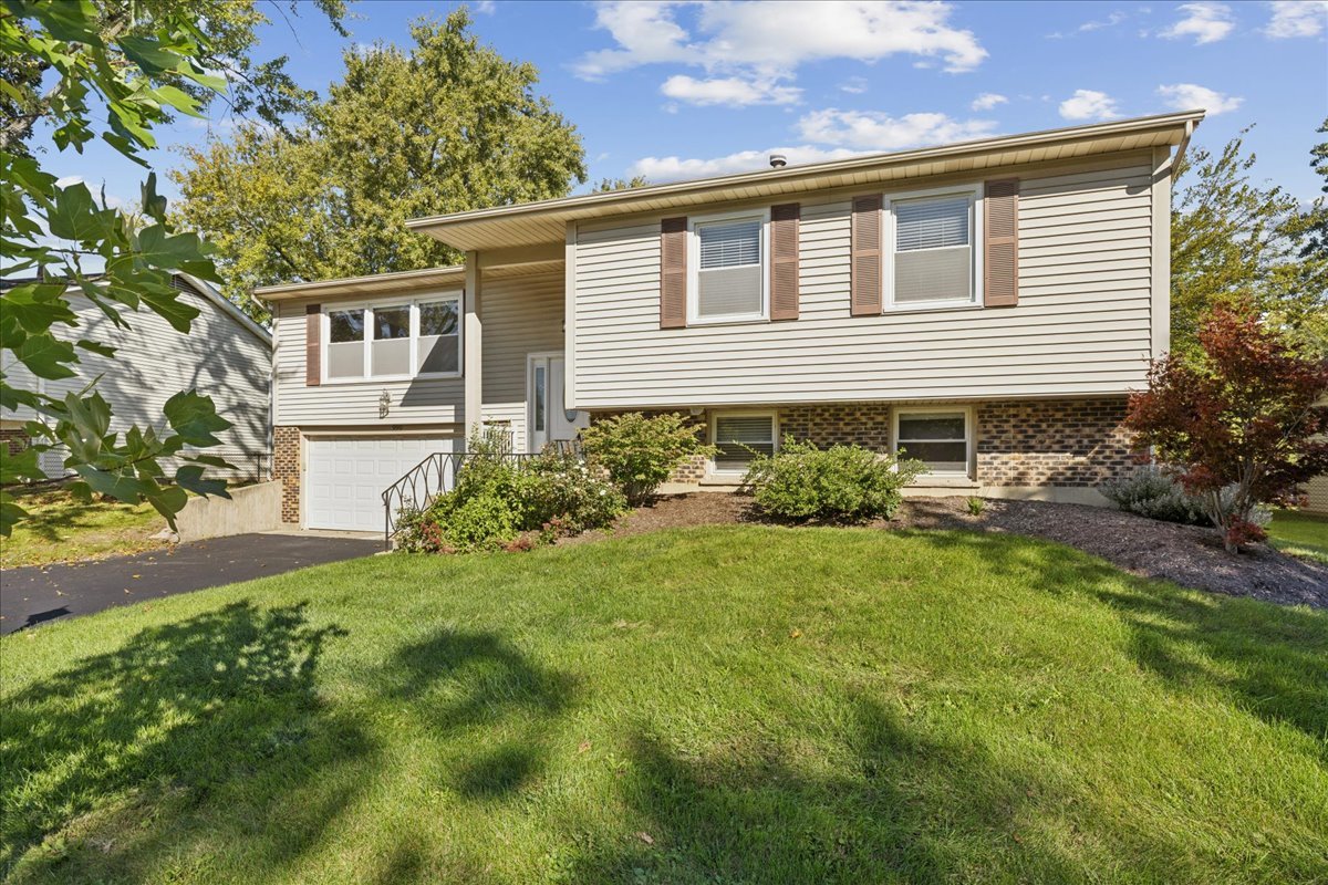 Split-level home with cream siding, brown shutters, brick facade, and attached garage.