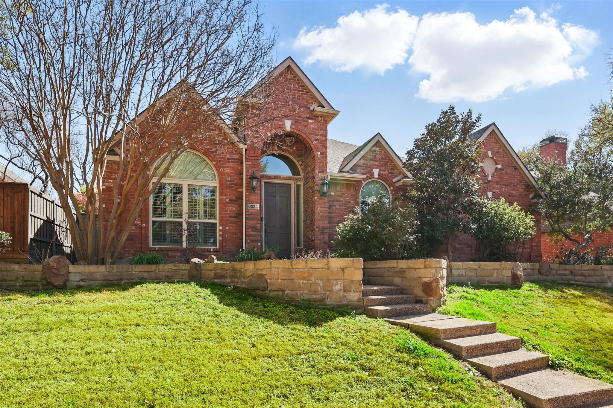Red-brick home with arched windows, a stone retaining wall, and front walkway.