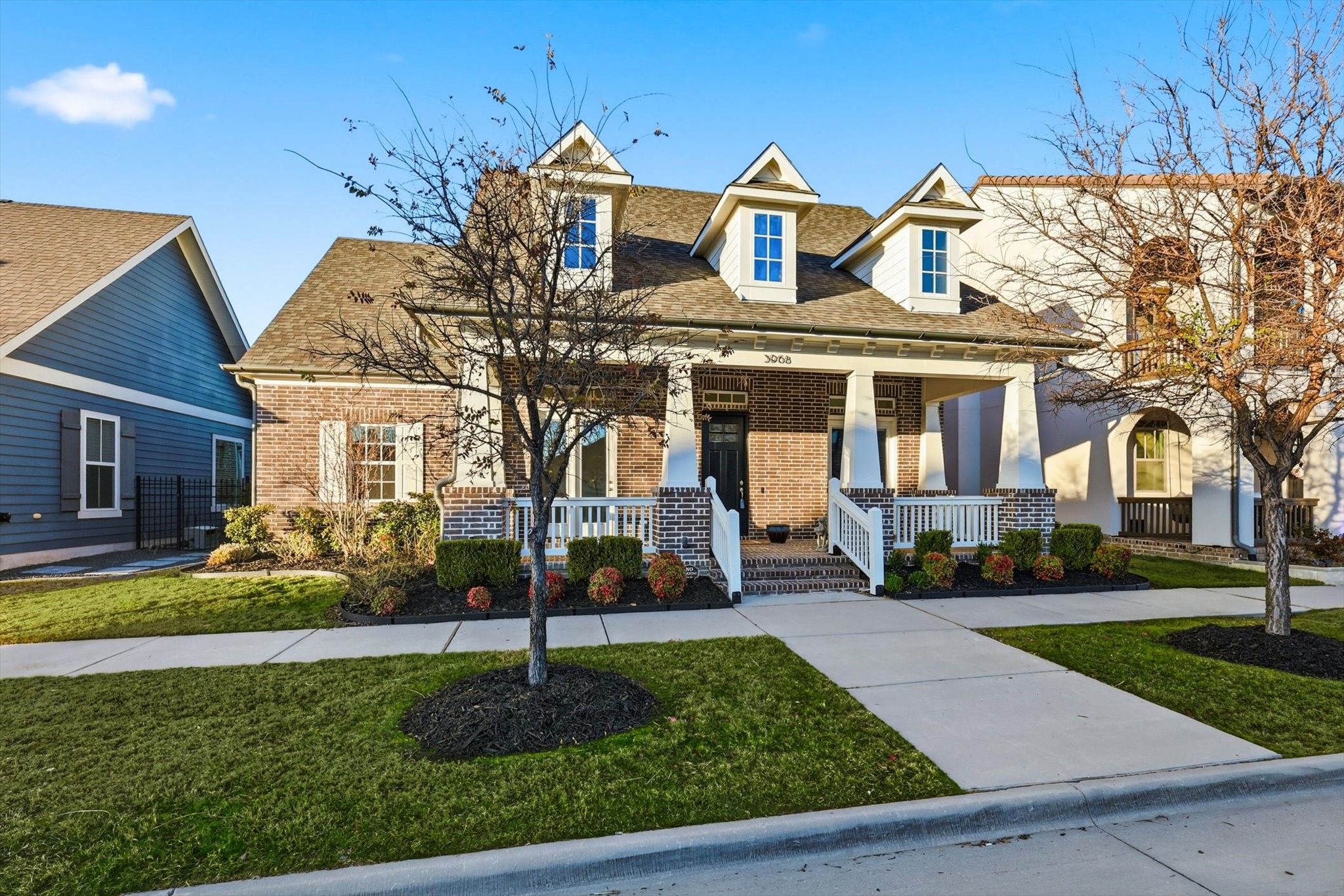 Two-story brick home with three dormers, a covered front porch, and landscaped lawn.