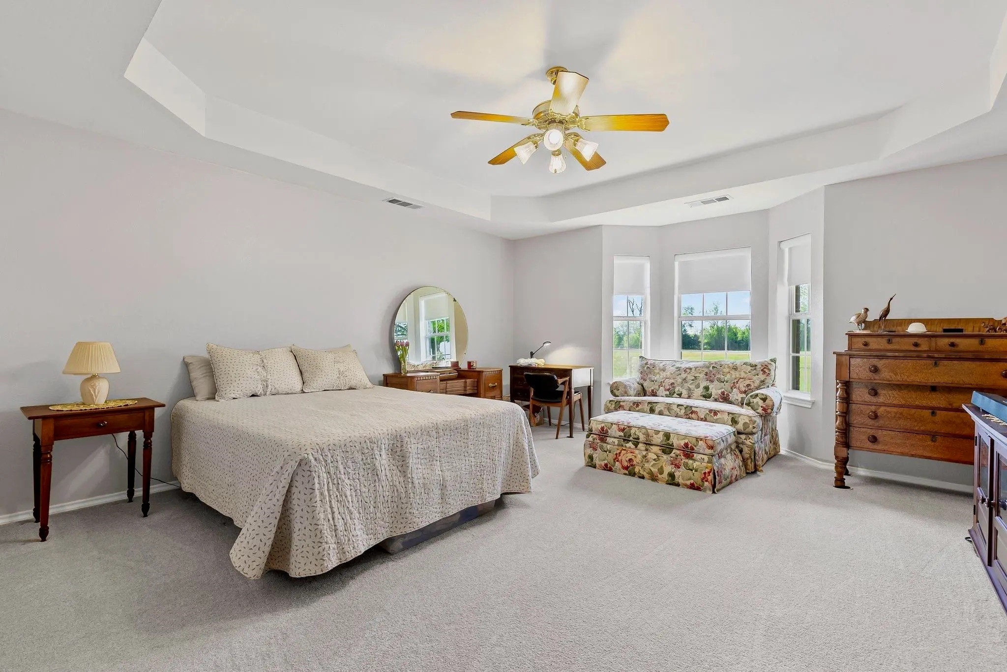 Furnished bedroom with a large bed, floral loveseat, and three windows.