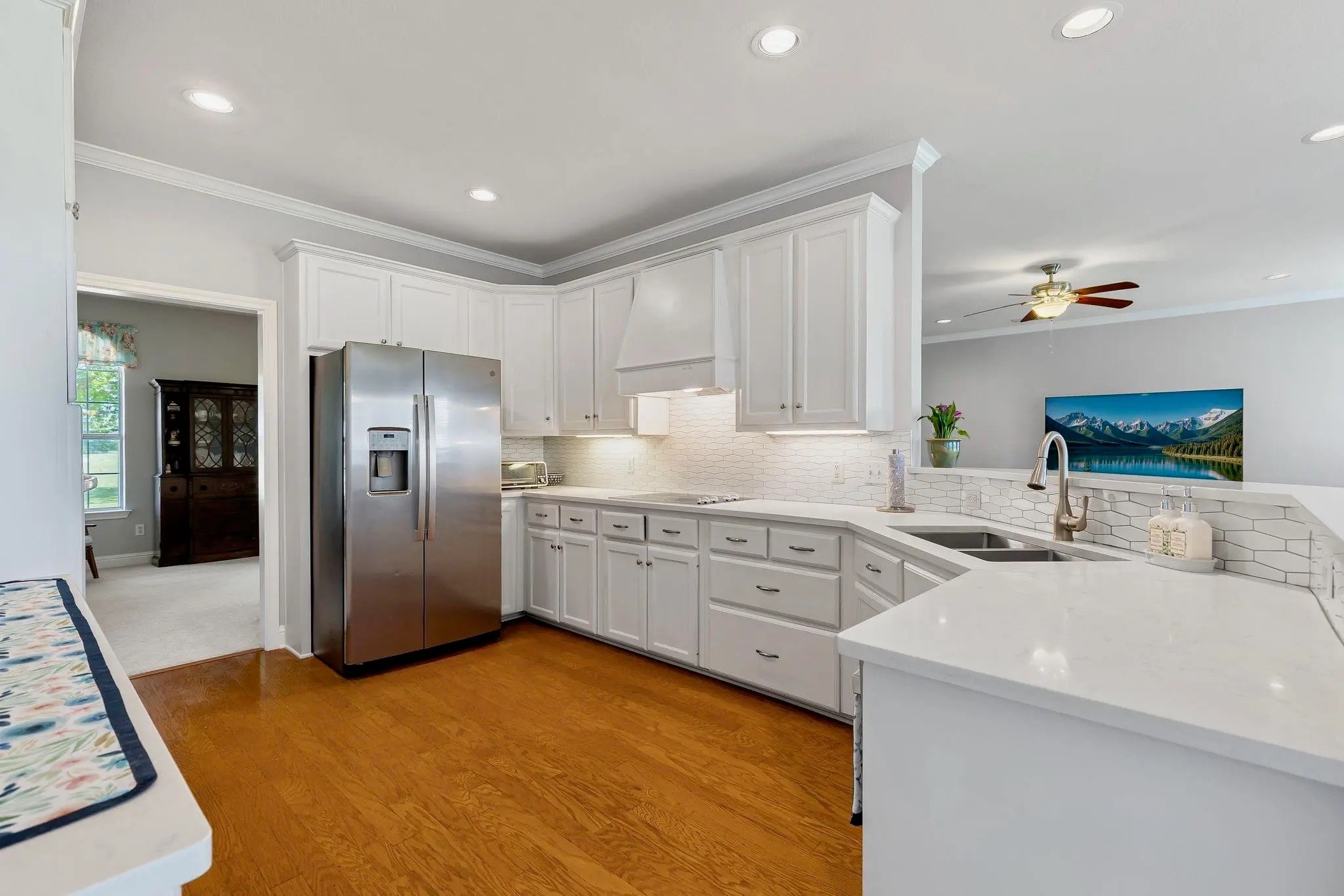 Bright kitchen with white cabinetry, hexagonal tile backsplash, stainless steel refrigerator, and a large peninsula.