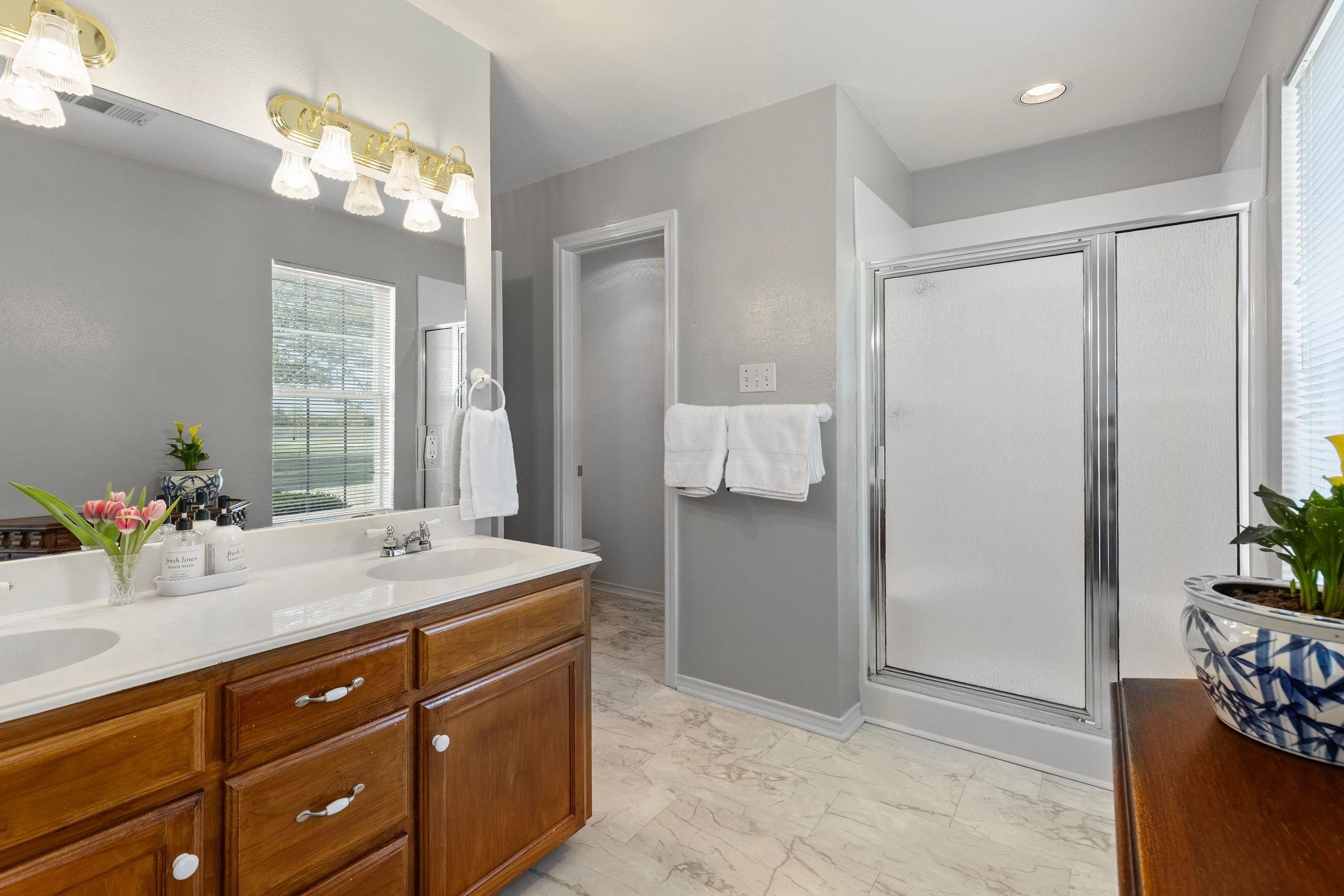 Bathroom with a wood double-sink vanity, large mirror, and frosted-glass shower.