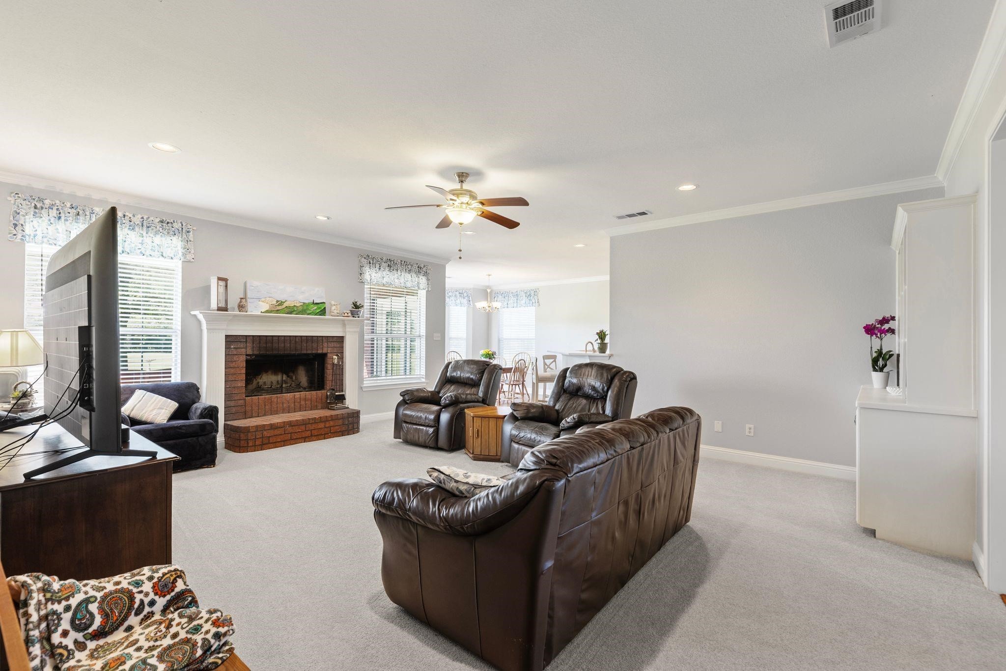 Furnished living room with brown leather seating, a brick fireplace, and an open dining area.