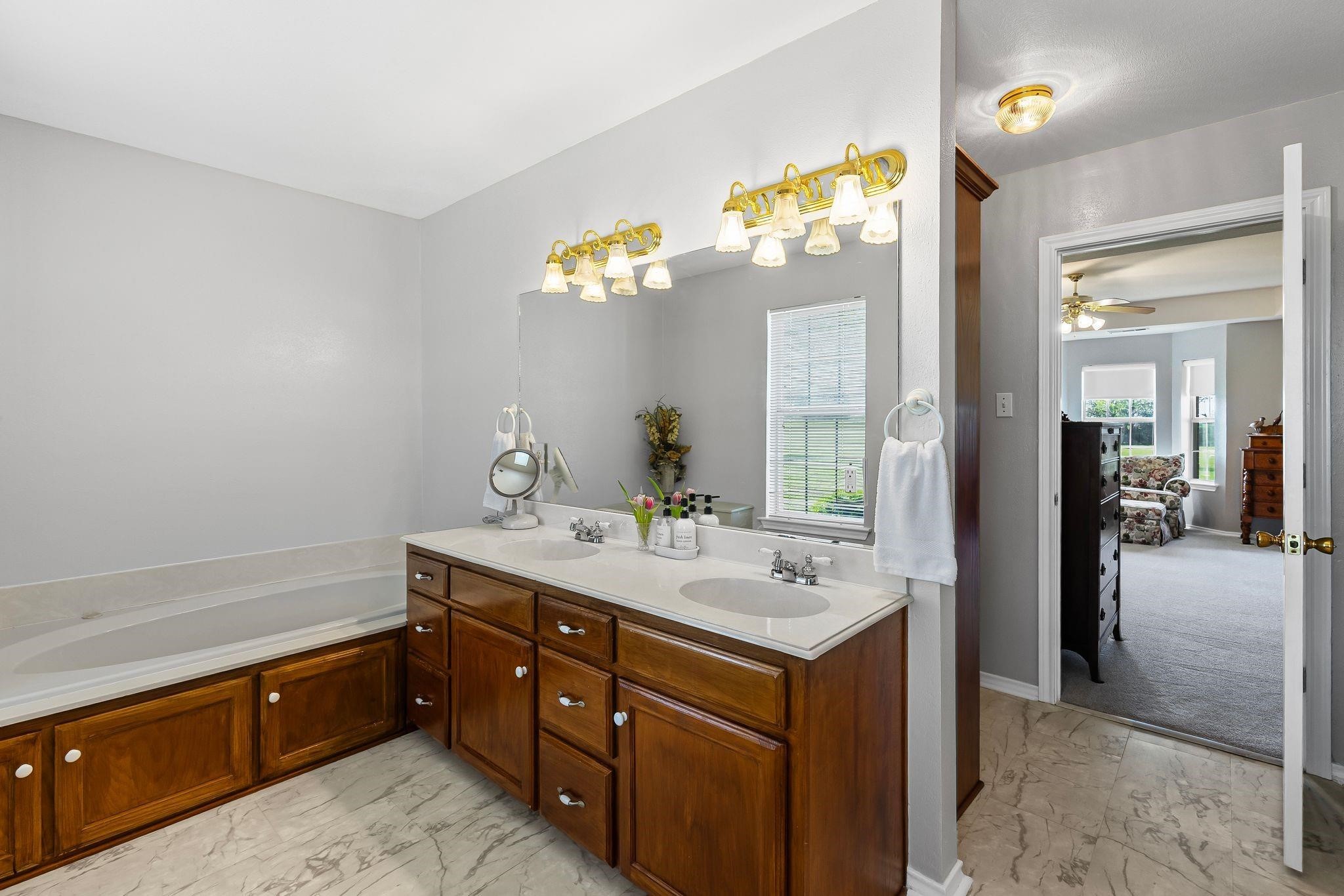 Bathroom with a built-in tub and long double vanity with dark wood cabinets and marble-look flooring.