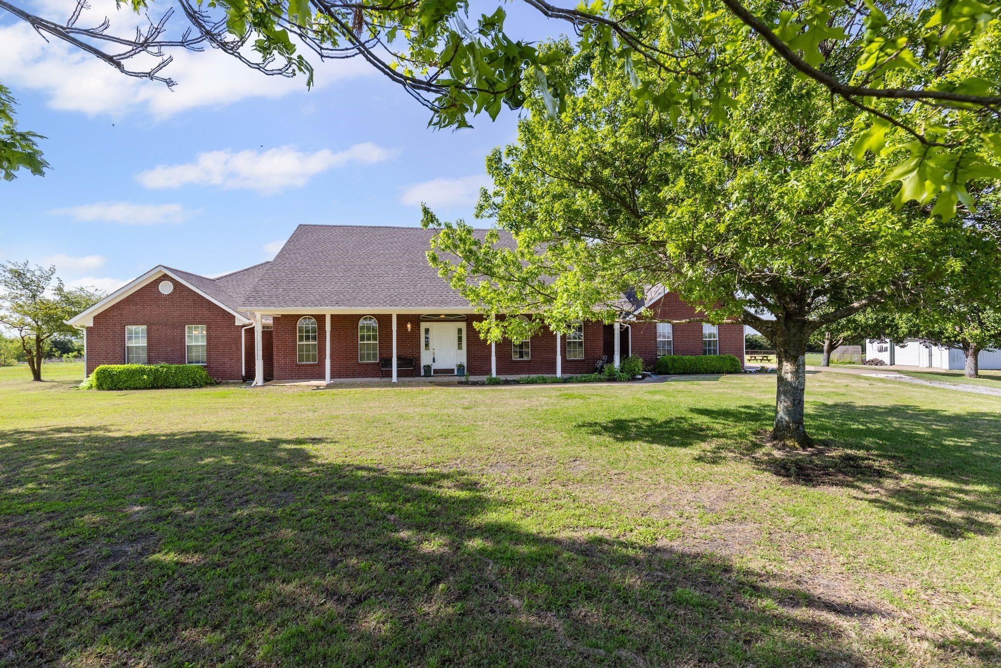 Red brick house with a covered porch, broad lawn, and mature shade trees.