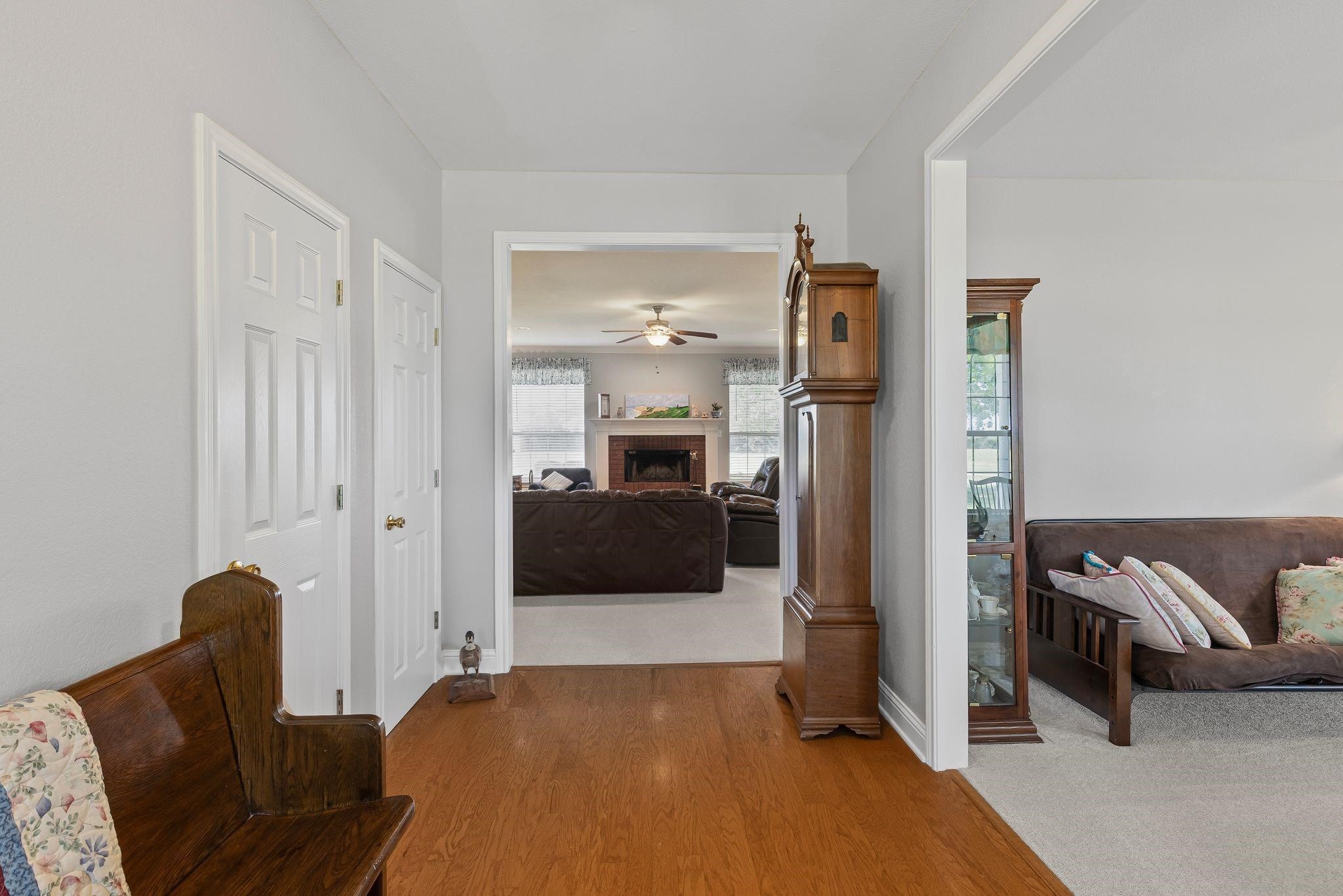 Furnished hallway with wood floors, opening onto living rooms with sofas and a fireplace.