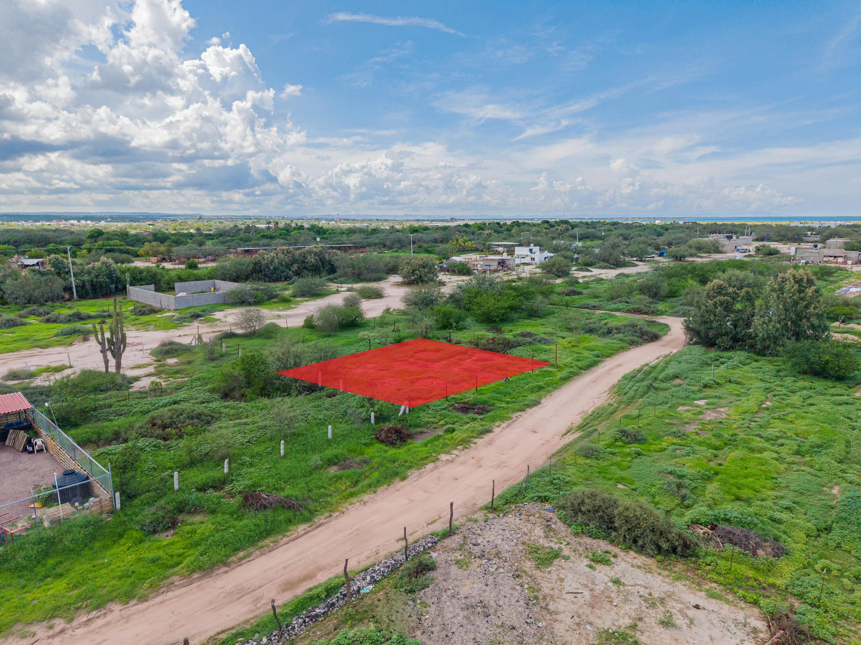 Vacant lot marked in red beside a dirt road, with distant water on the horizon.