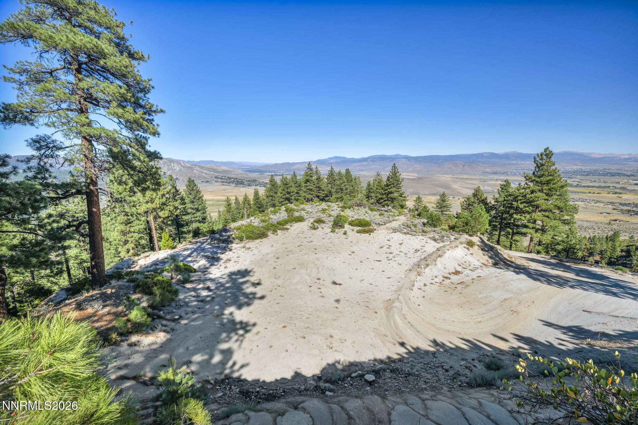 Sandy hillside property with pine trees overlooking a wide valley and mountain ranges.