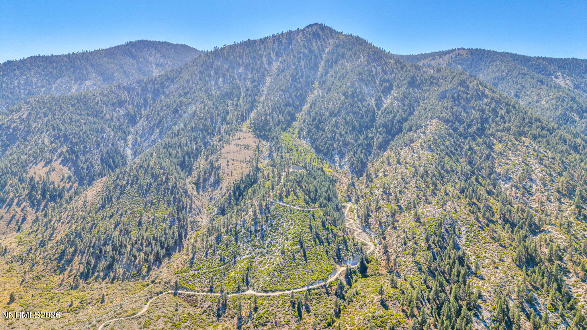Aerial view of rugged mountain terrain with a winding dirt road and forested ridge.