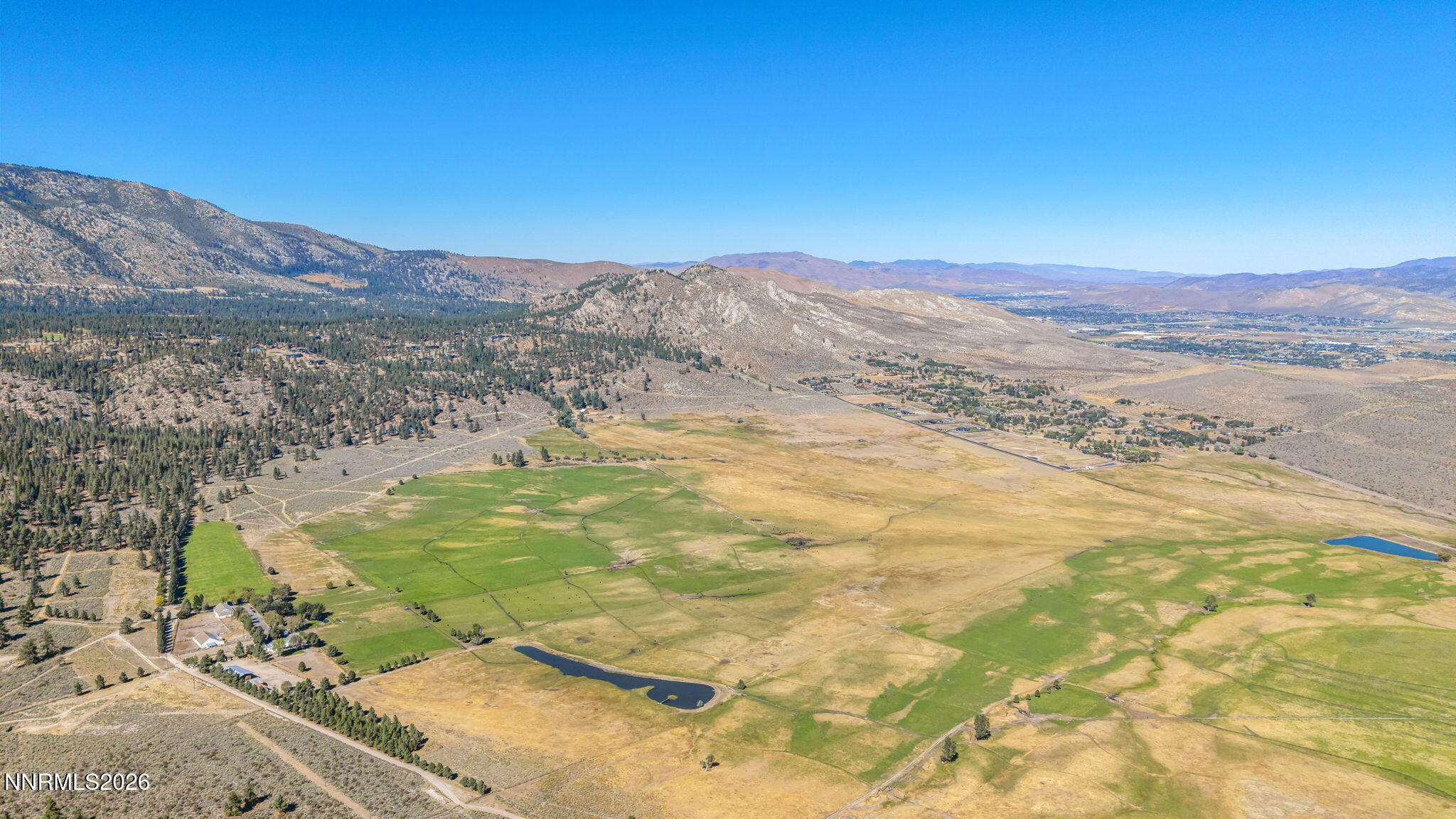 Aerial view of a rural valley with fields, ponds, scattered buildings, and mountains.