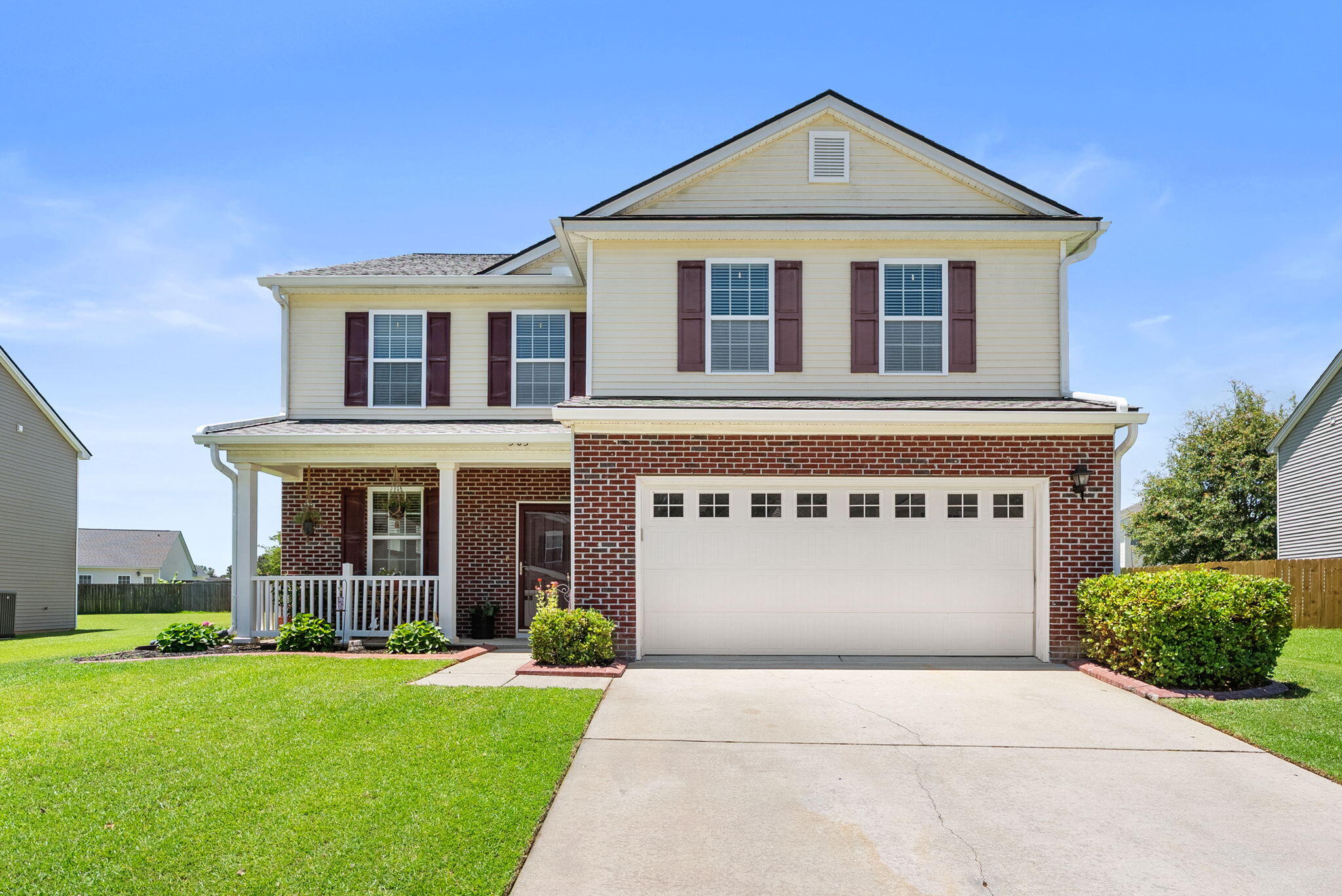 Two-story cream-sided and brick house with a covered porch, attached garage, and broad driveway.