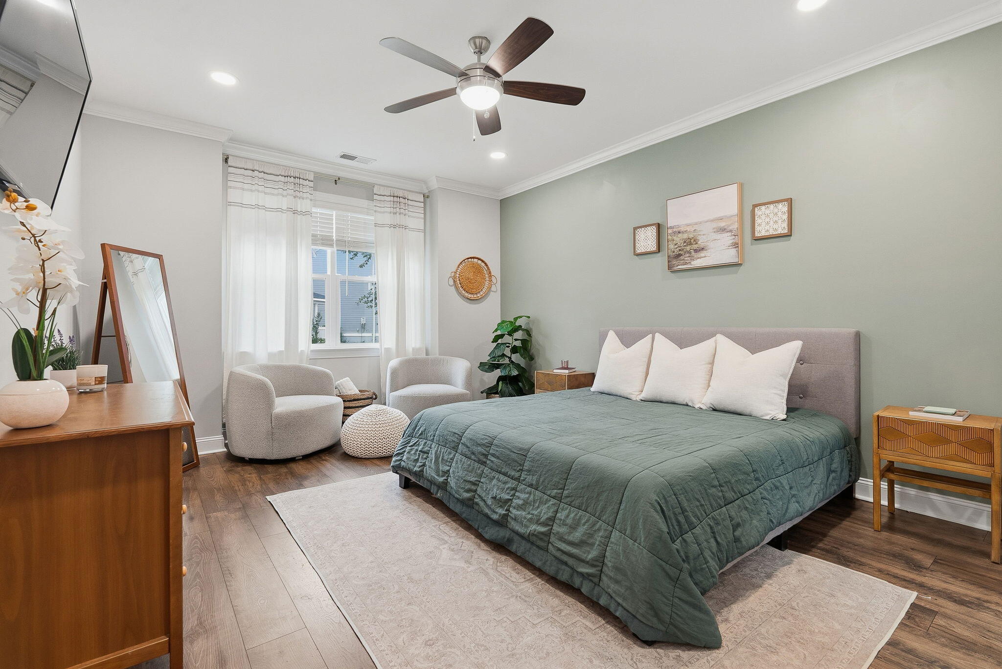 Staged bedroom with a green-quilted bed, pale green accent wall, and two chairs by the window.