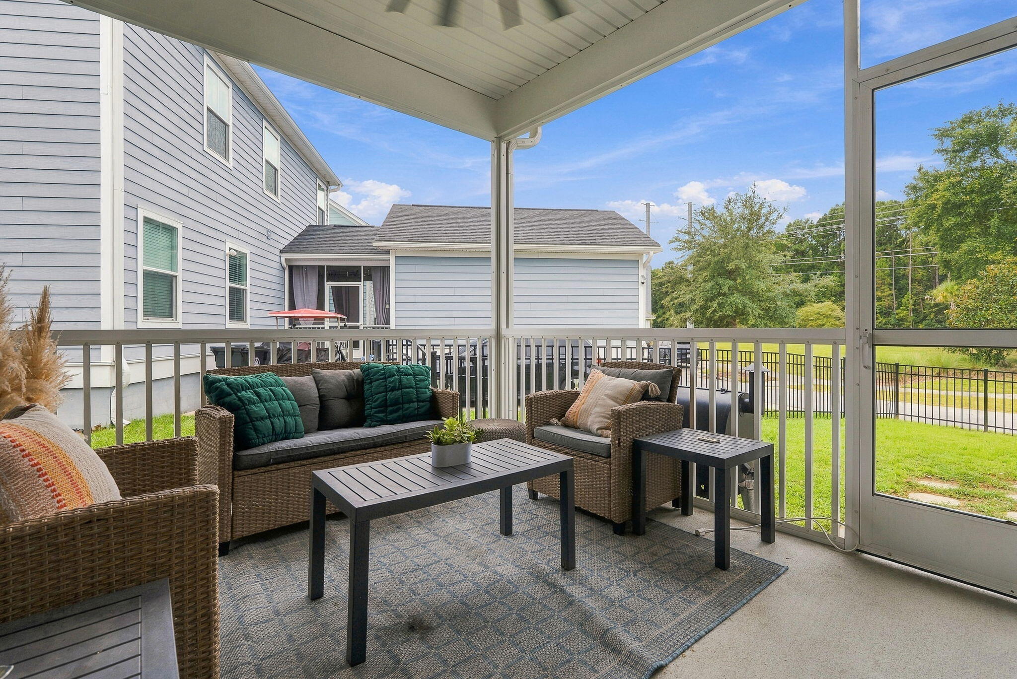 Screened porch with wicker seating and teal cushions overlooking a green lawn.