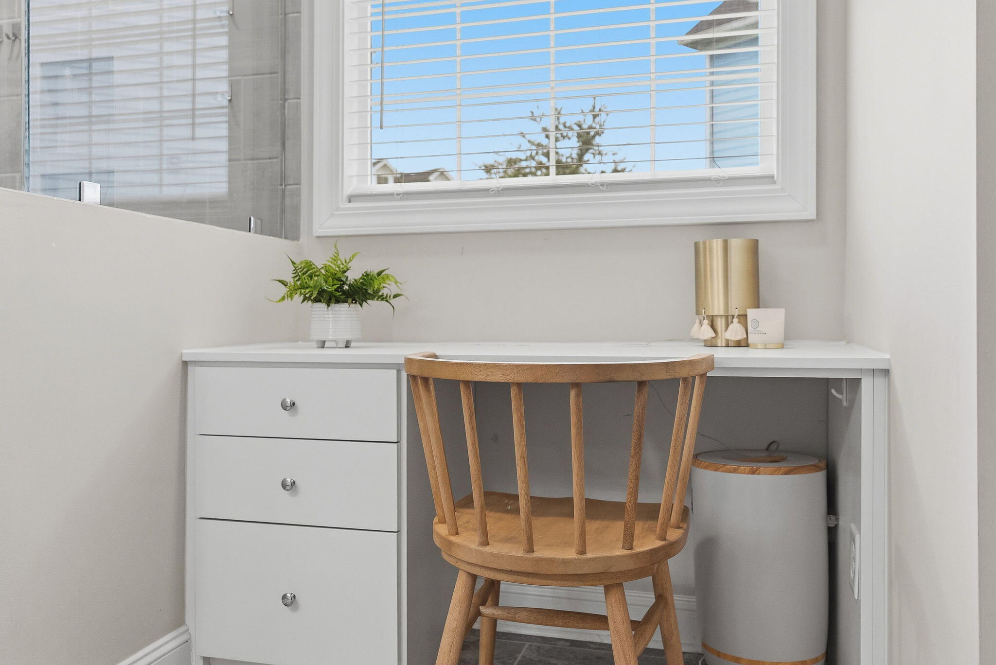Bright built-in desk beneath a large window, with a wooden chair and potted fern.