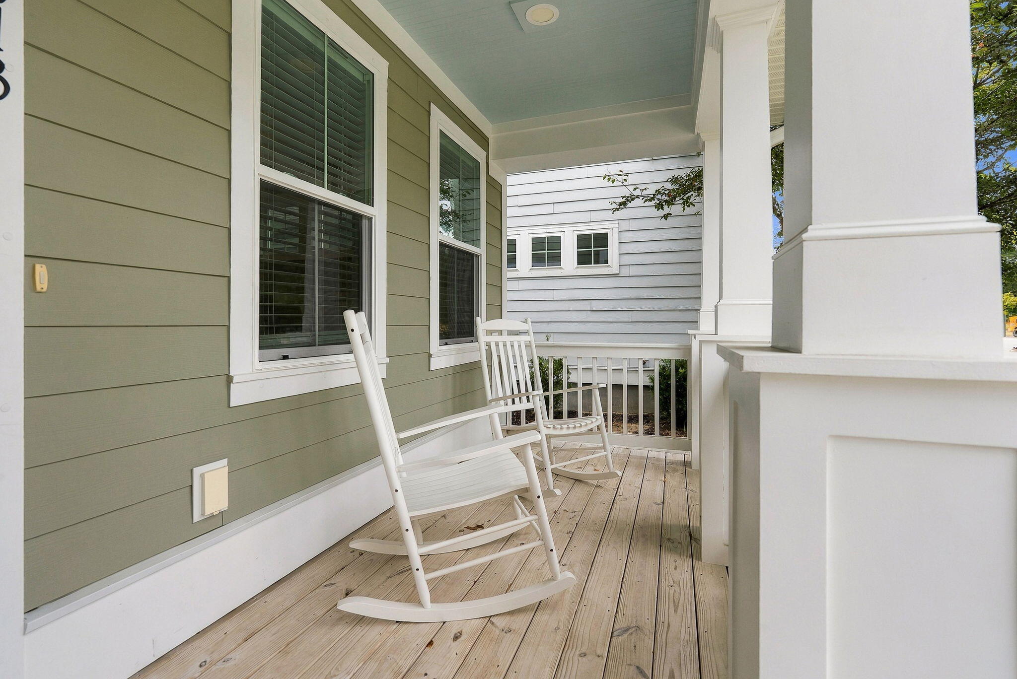 Covered porch with two white rocking chairs, sage-green siding, and white columns.