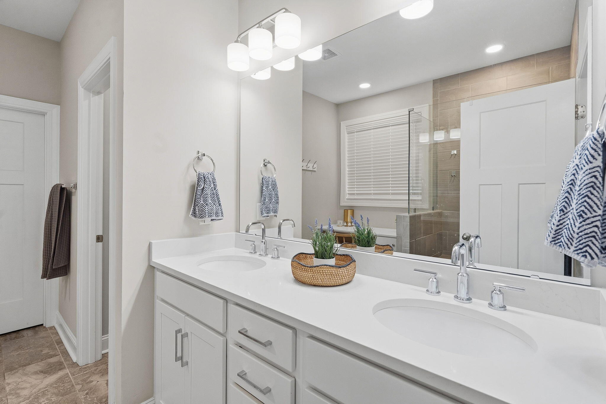 Bathroom with a double-sink vanity, large mirror, and glass shower with beige tile.