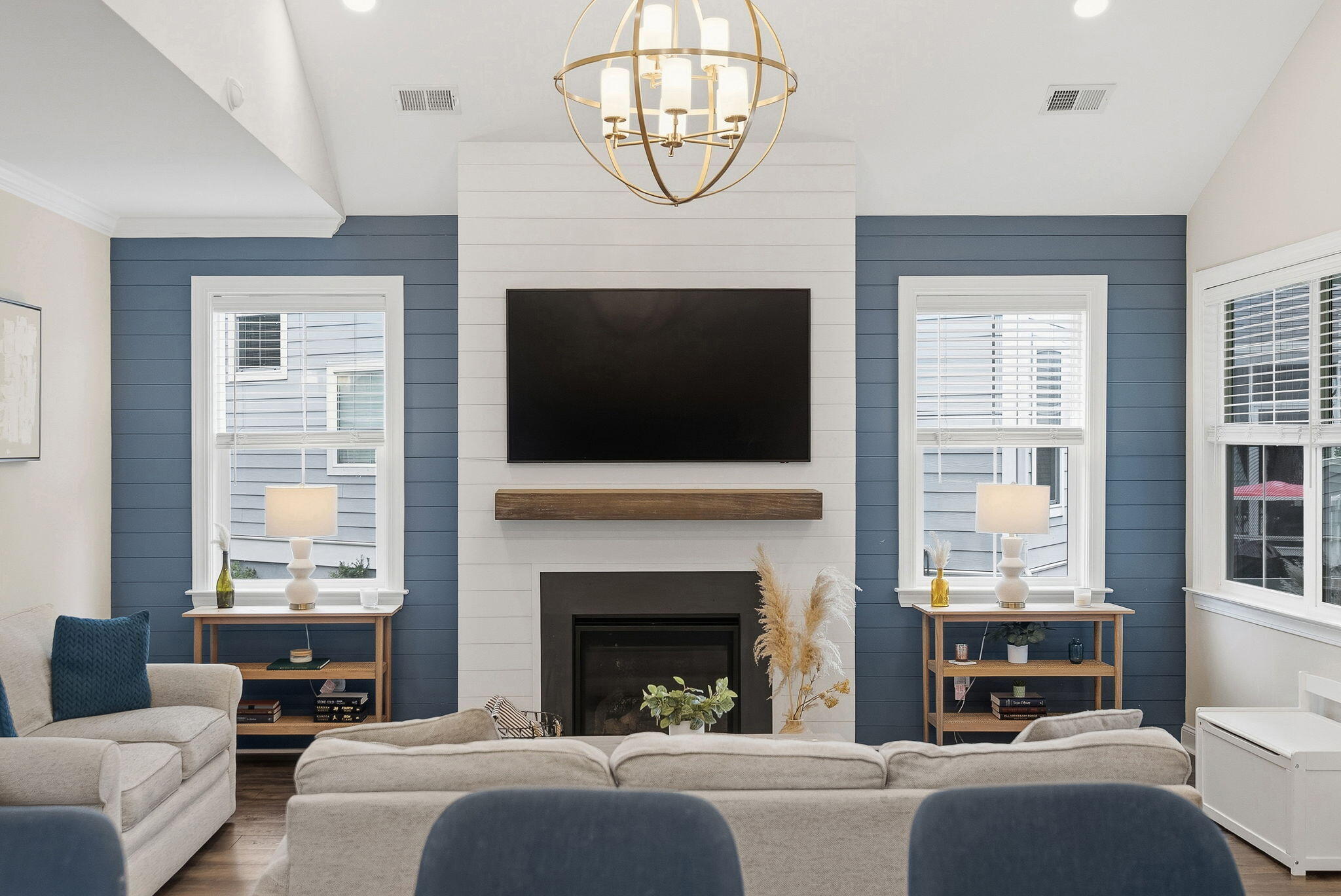 Living room with a white shiplap fireplace, mounted television, blue paneled walls, and light sofas.
