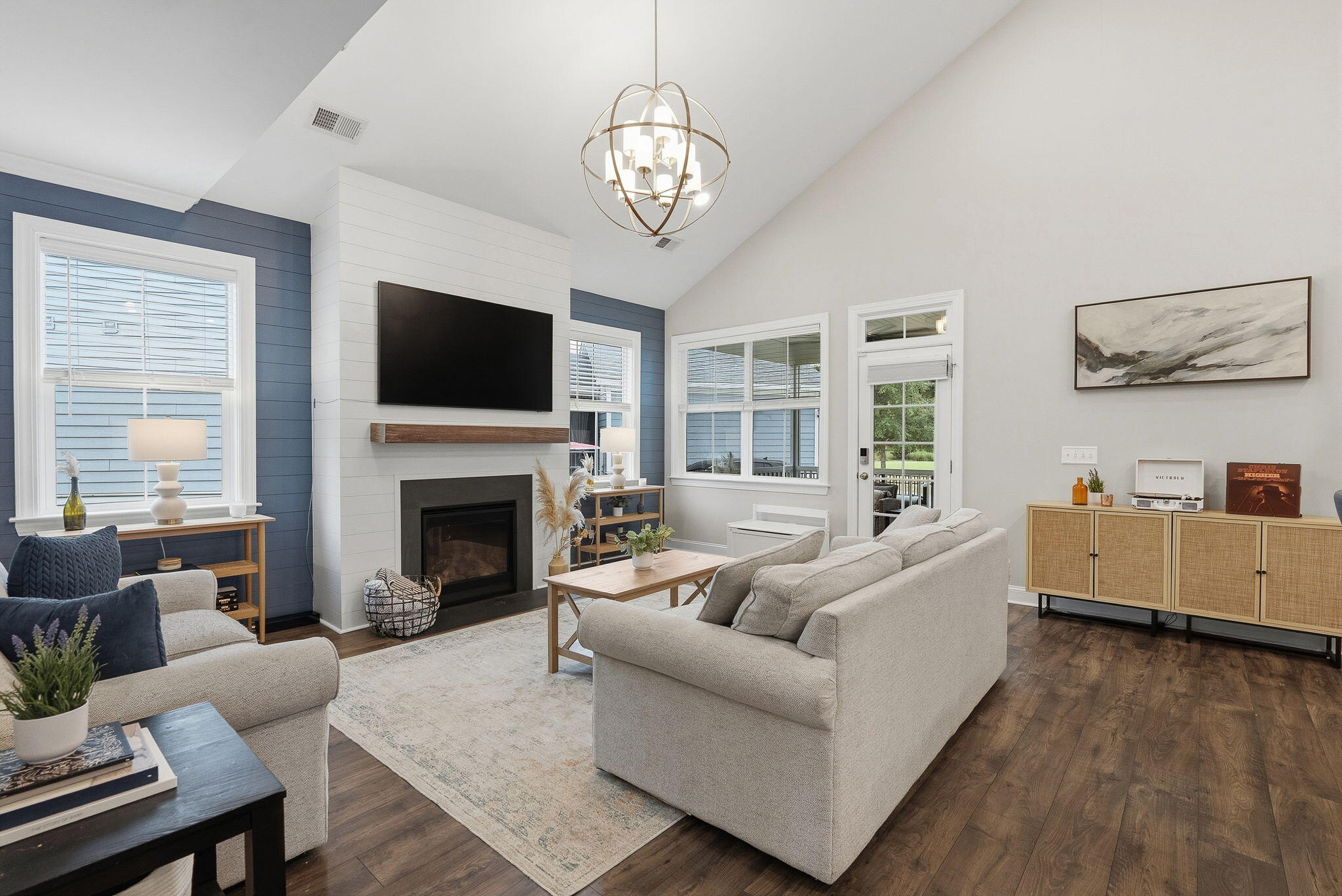 Staged living room with a vaulted ceiling, fireplace, blue accent walls, and large windows.