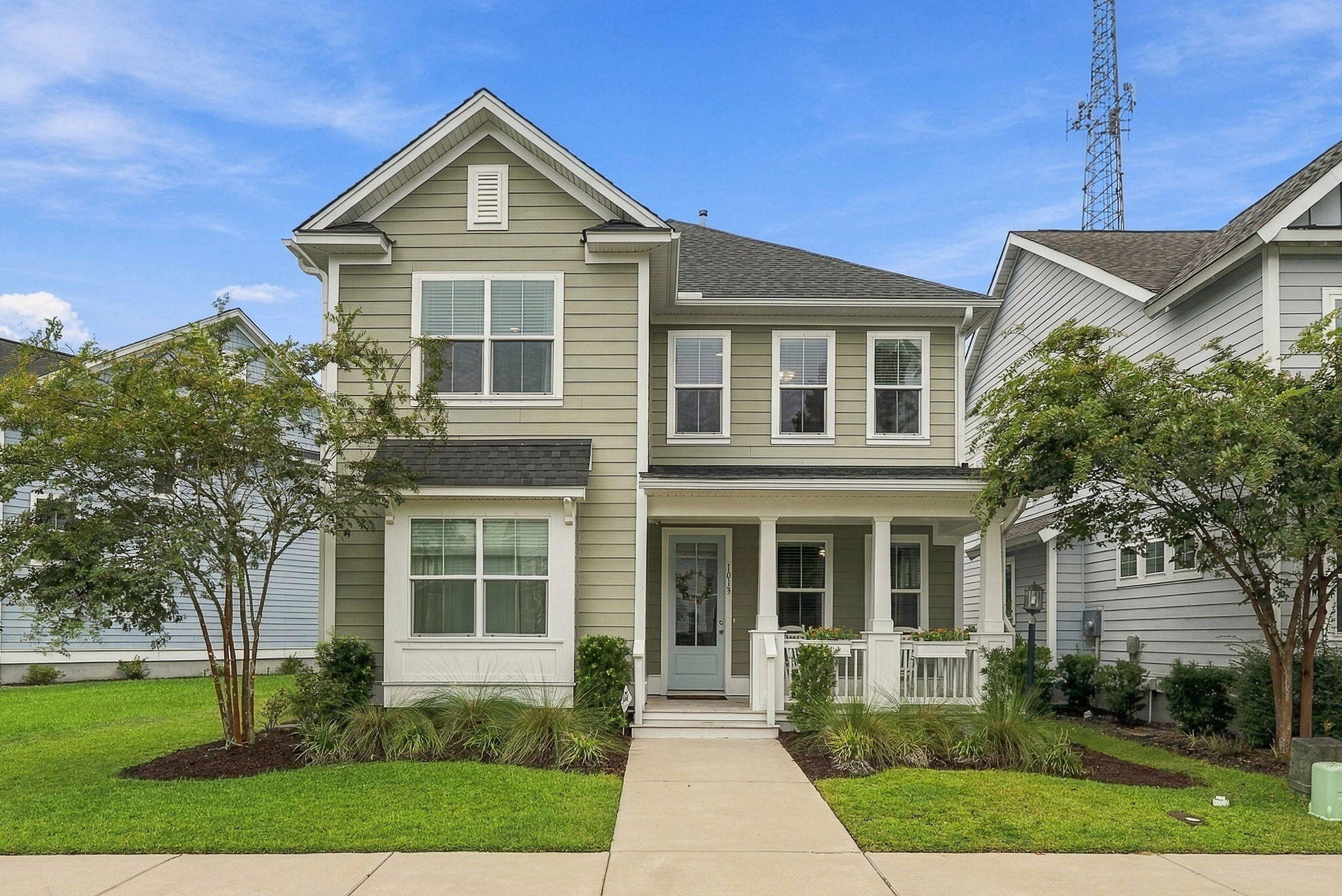 Sage-green two-story house with a covered porch, front walkway, and landscaped lawn.