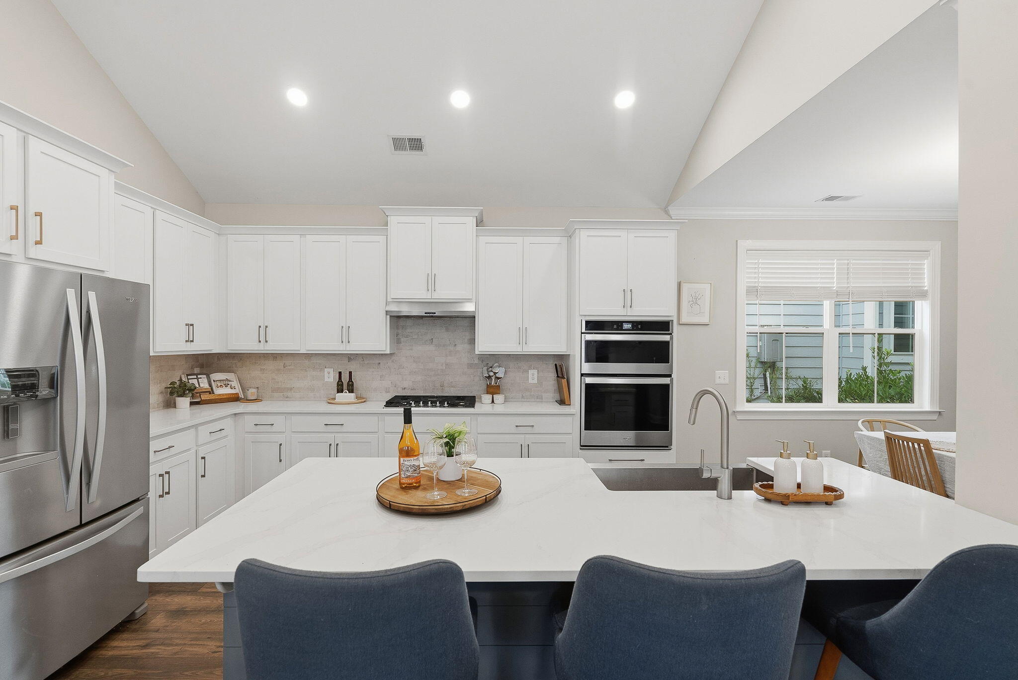 Bright kitchen with white cabinets, stainless appliances, and a large island with dark bar stools.