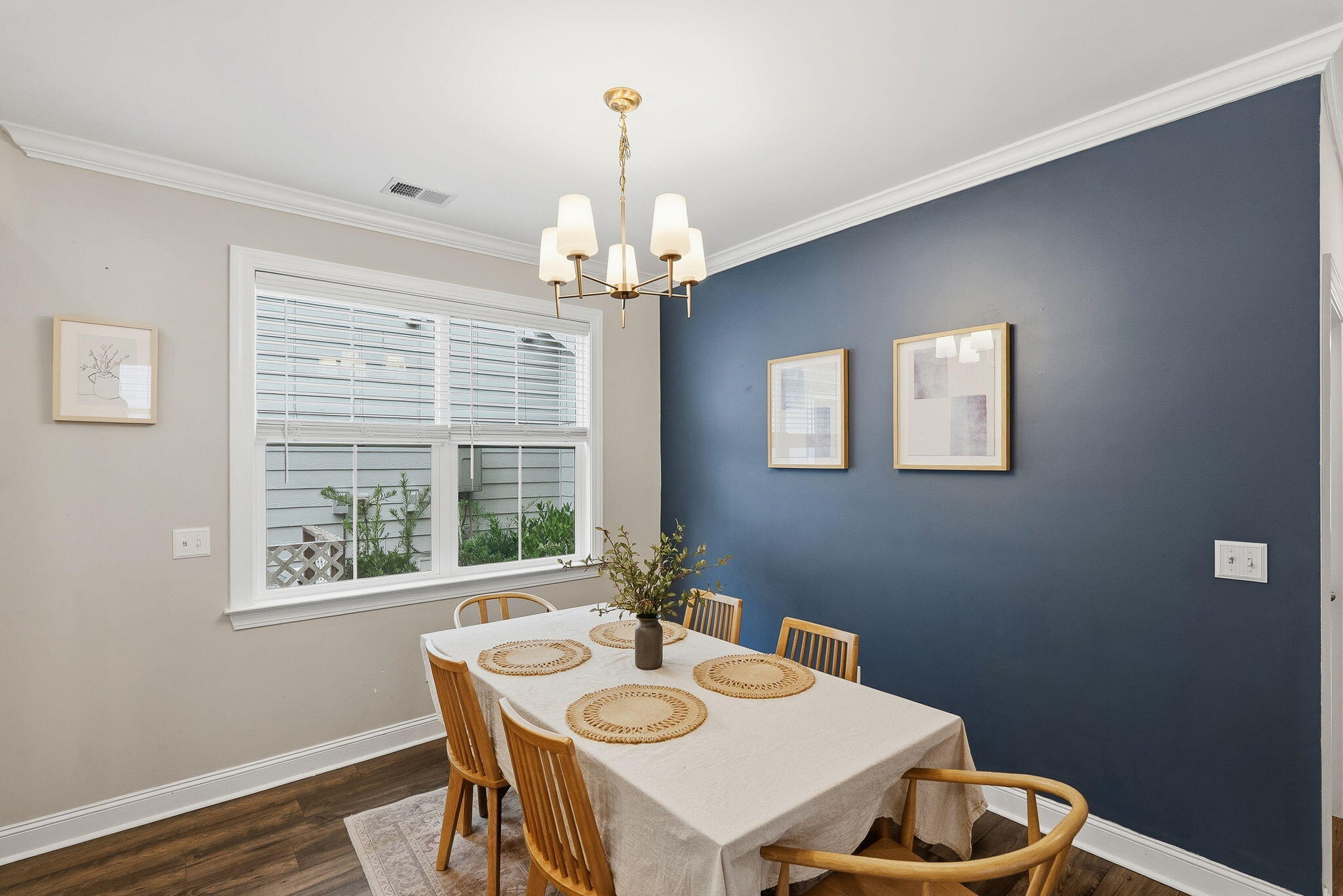 Dining room with a navy accent wall, wooden chairs, and a brass chandelier above a set table.