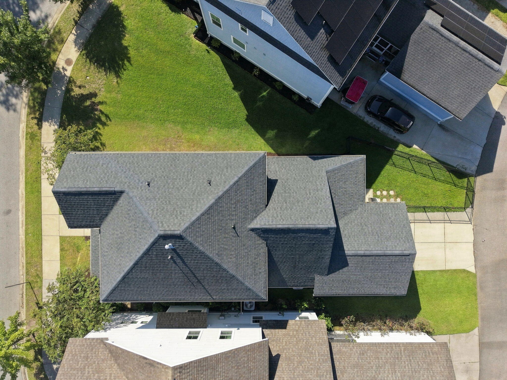 Aerial view of a gray-shingled home surrounded by lawn, sidewalks, and a fenced side yard.