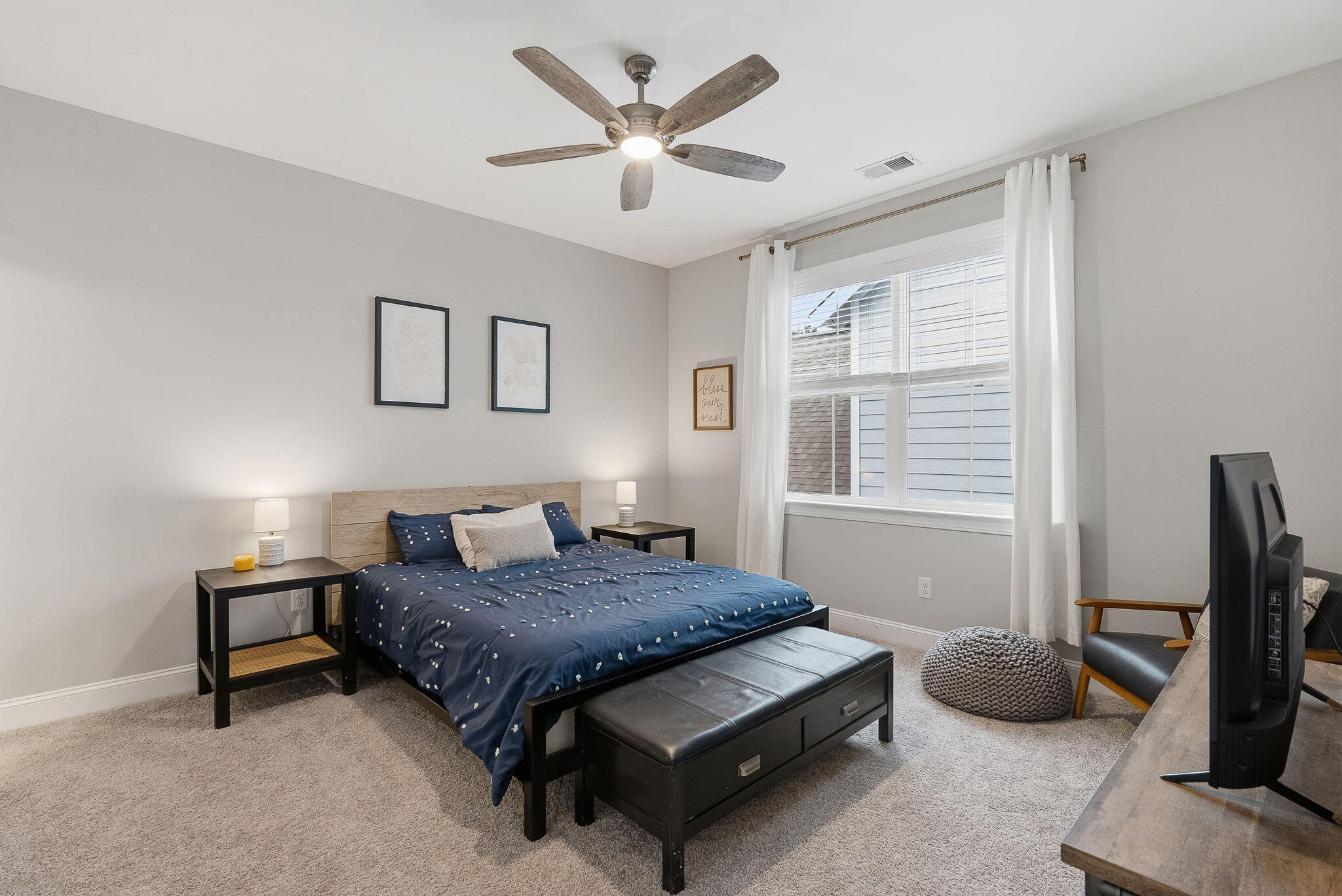 Bedroom with navy bedding, a black storage bench, and a large curtained window.