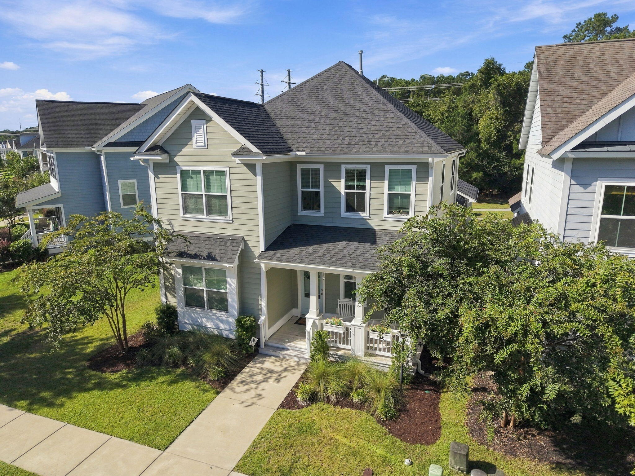 Two-story gray-green house with white trim, a covered porch, and landscaped front yard.