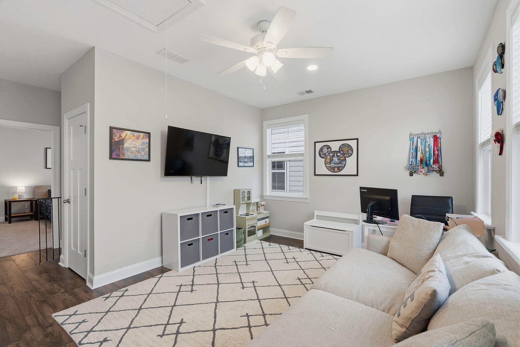 Family room with a large sectional, wall-mounted TV, children’s play kitchen, and medals on display.