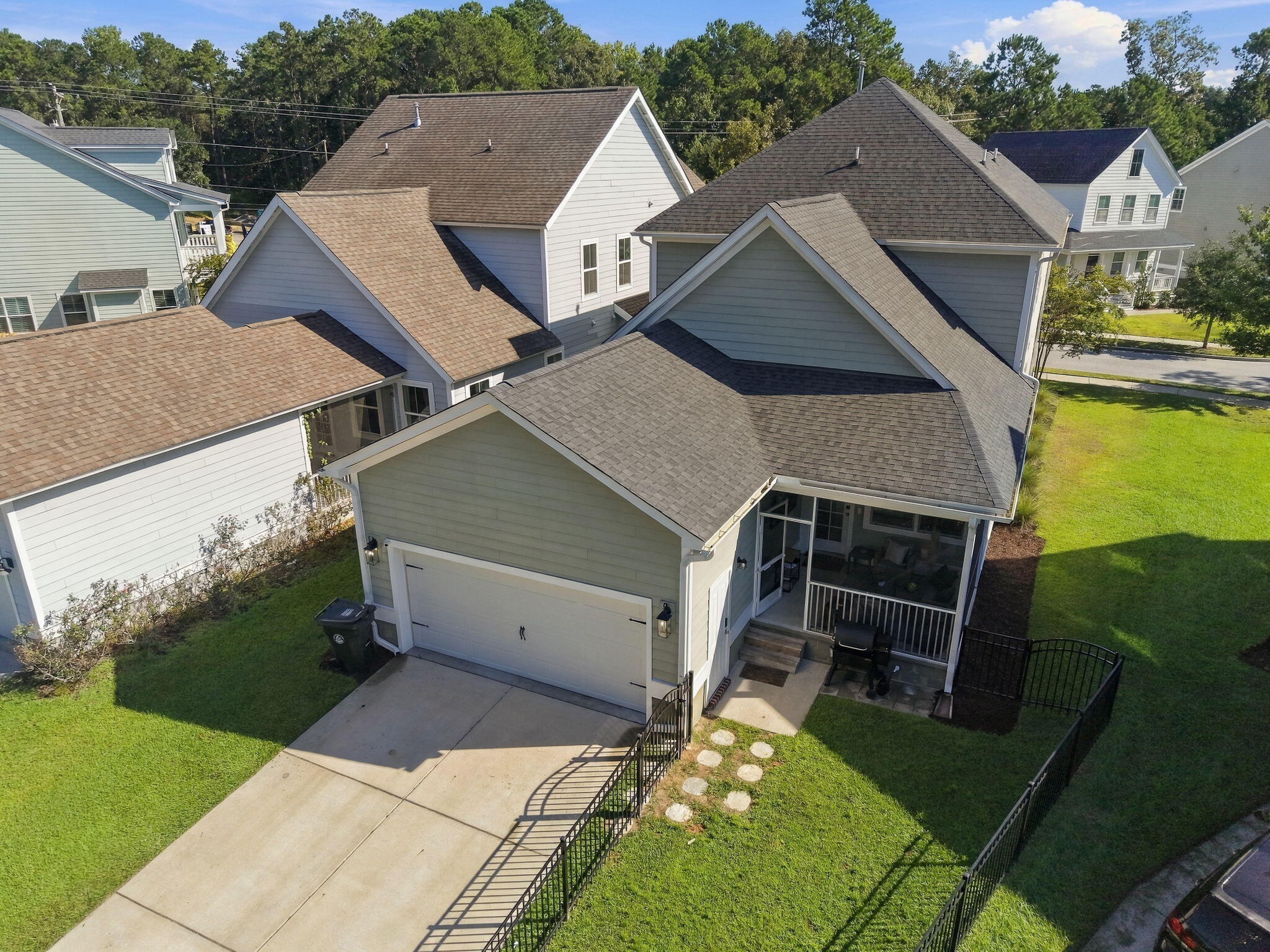 Aerial view of a gray house with a two-car garage, screened porch, and fenced lawn.