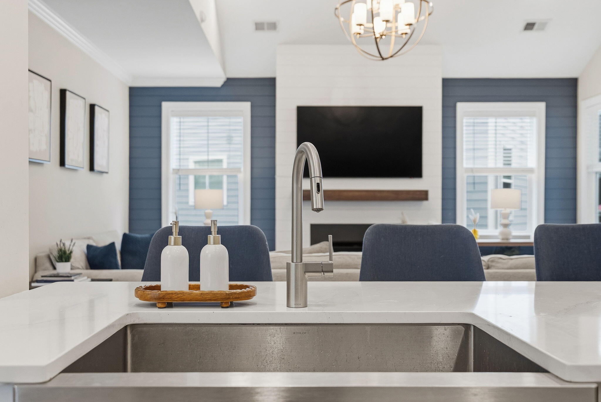 Kitchen sink and white island facing a living room with a fireplace and blue accent wall.
