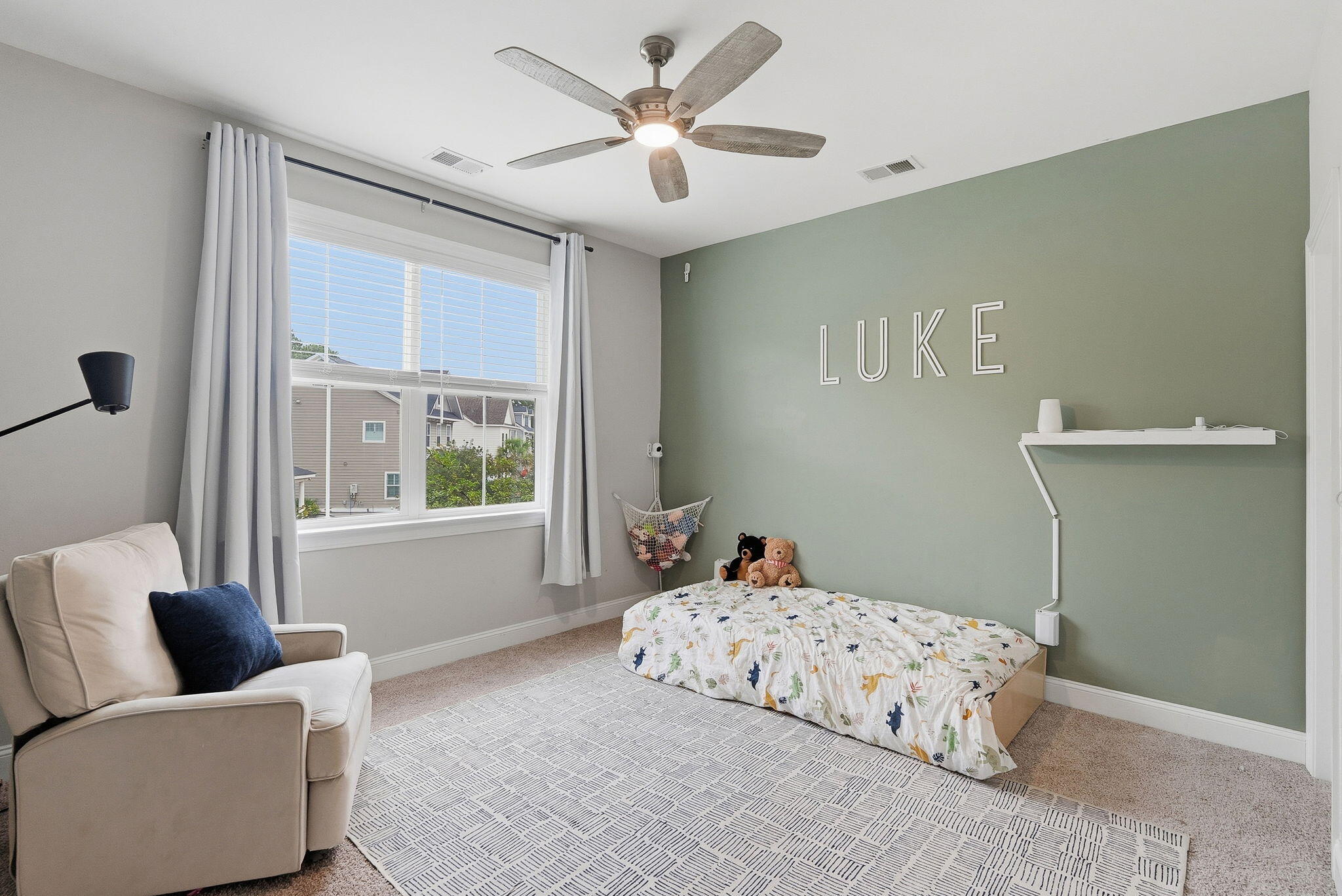 Bedroom with dinosaur-print bedding, a sage-green accent wall, and a large curtained window.