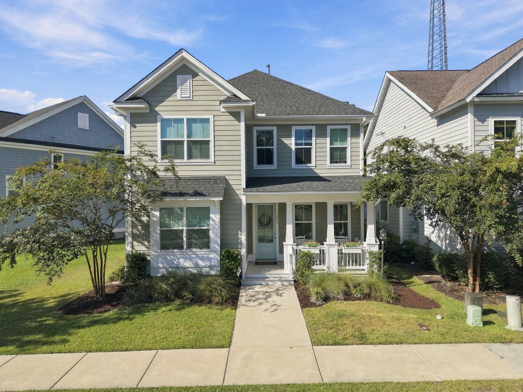 Two-story gray-green house with a white-trimmed covered porch, white seating, and landscaped front lawn.