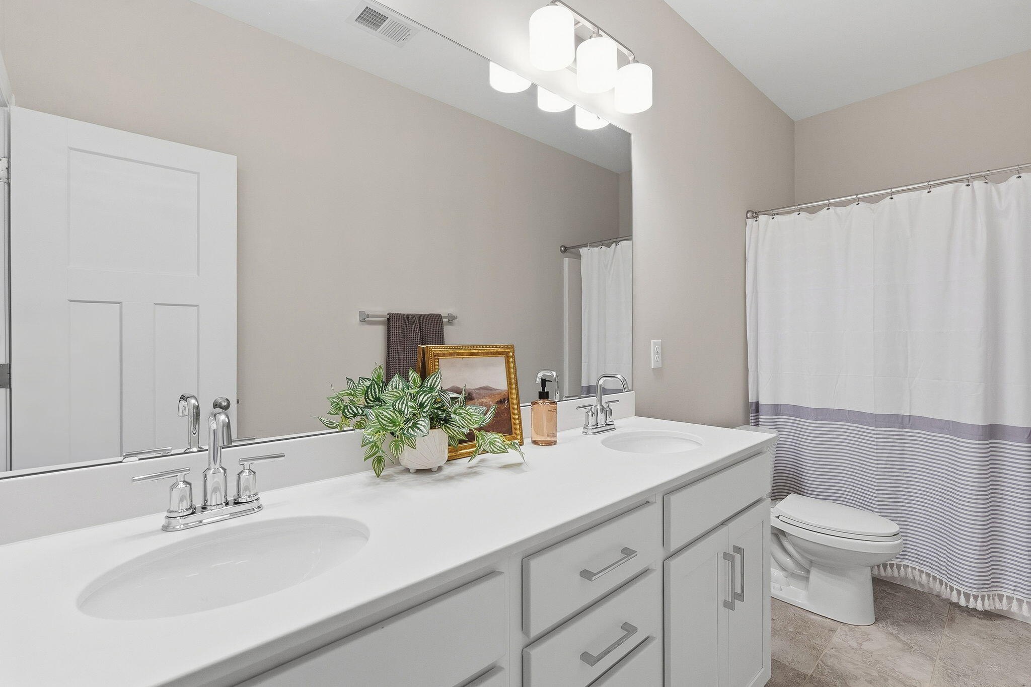 Bathroom with double-sink vanity, large mirror, and white shower curtain with gray stripes.