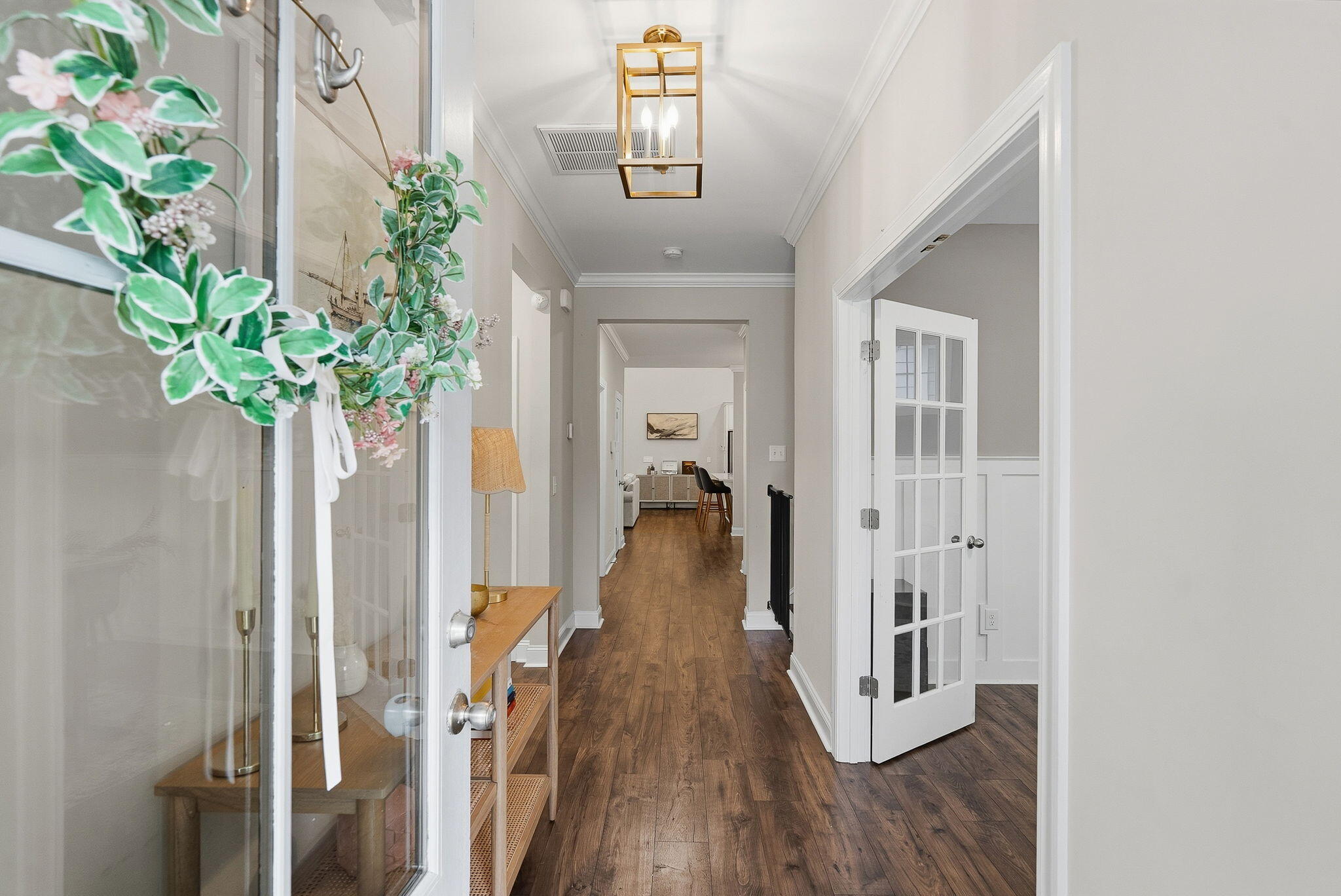 Furnished entry hallway with dark wood floors, a brass pendant light, and an open glass-paneled door.