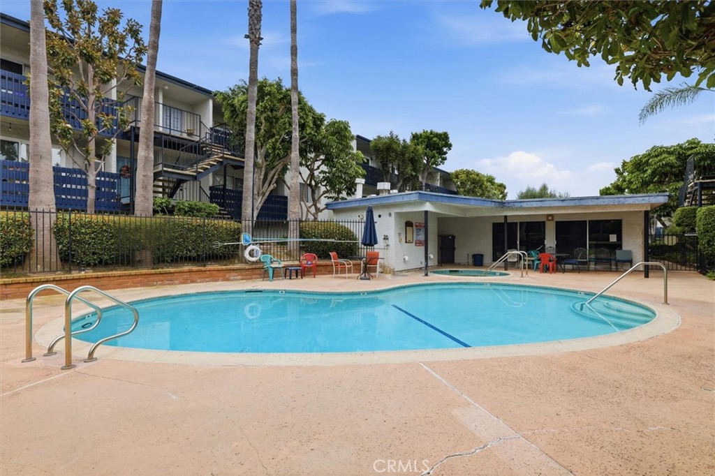 Community swimming pool with curved blue water, metal handrails, and a covered lounge area.