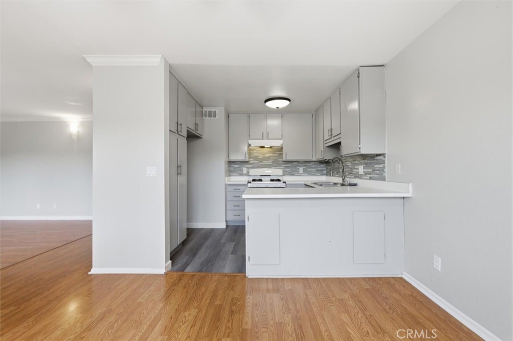 Kitchen with white cabinets, gray tile backsplash, and a peninsula counter beside wood-look flooring.