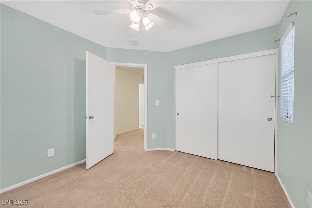 Empty bedroom with beige carpet, sliding closet doors, and a ceiling fan.
