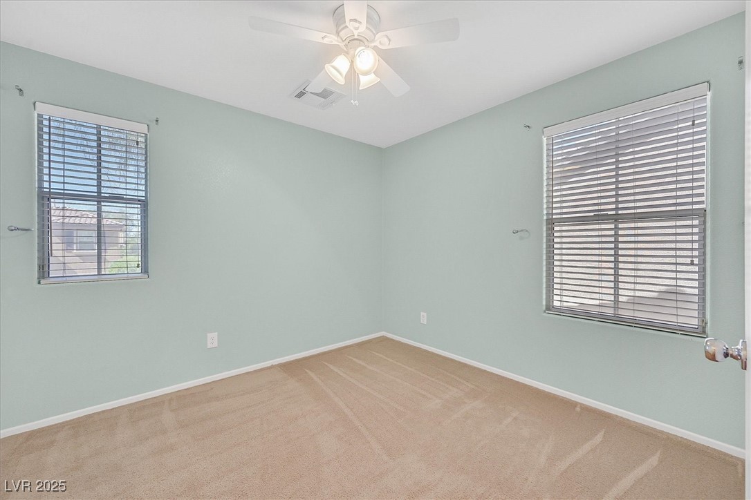 Empty bedroom with pale green walls, beige carpet, two blinded windows, and a ceiling fan.