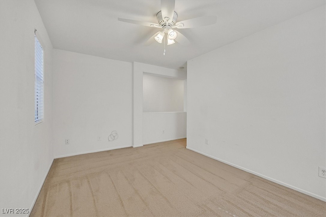 Empty carpeted bedroom with a ceiling fan and narrow window with blinds.