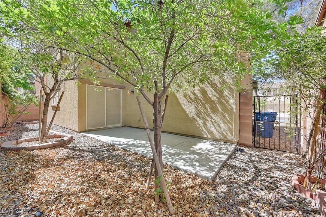 Backyard patio shaded by mature trees, with a concrete slab, sliding glass door, and rock landscaping.