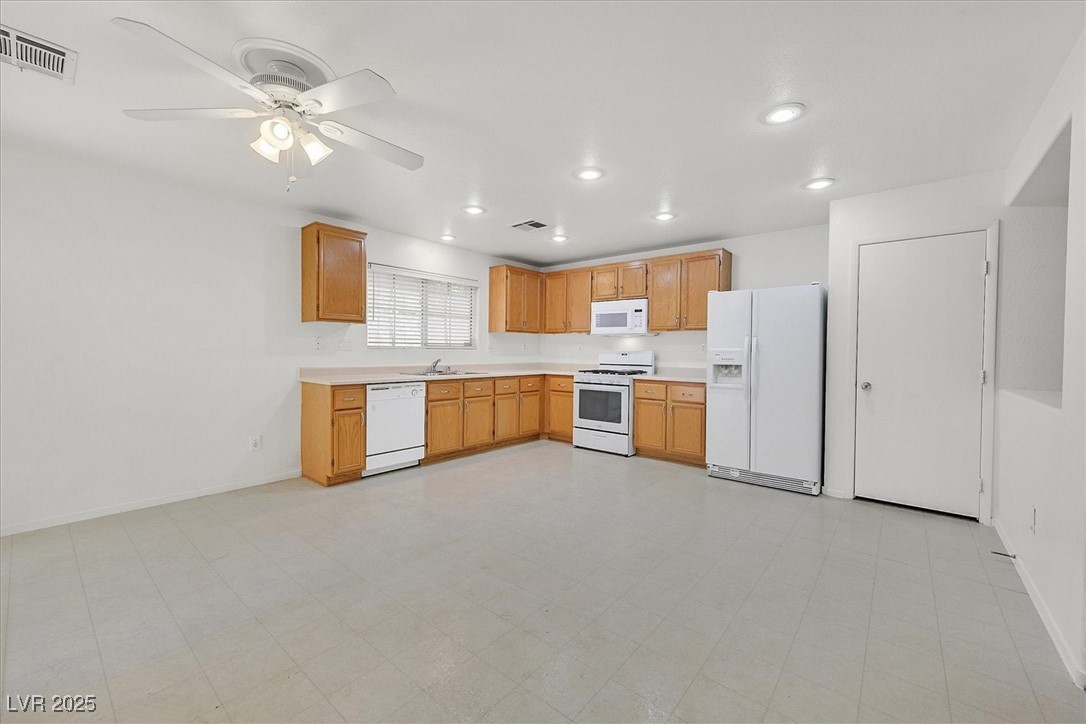 Empty kitchen with honey-colored cabinets, white appliances, and a ceiling fan.