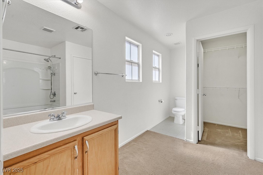 Bathroom with a wood vanity, tub and shower, toilet, and open walk-in closet.