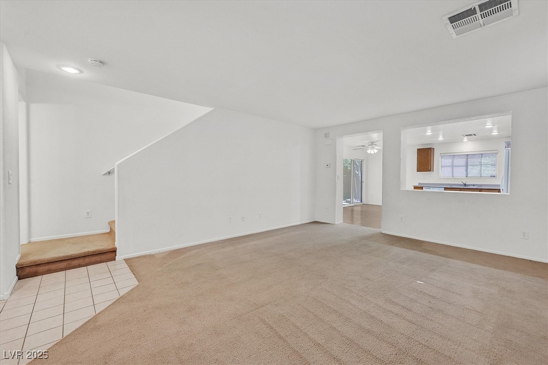 Vacant living room with beige carpet, tiled entry, short staircase, and pass-through opening to the kitchen.