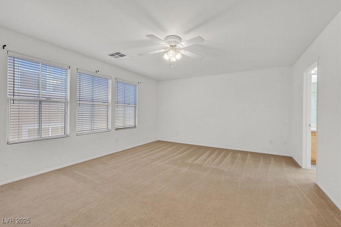 Vacant carpeted bedroom with three blind-covered windows and a ceiling fan.